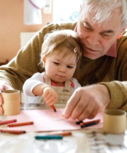 An older man sitting at a table with little girl and coloring